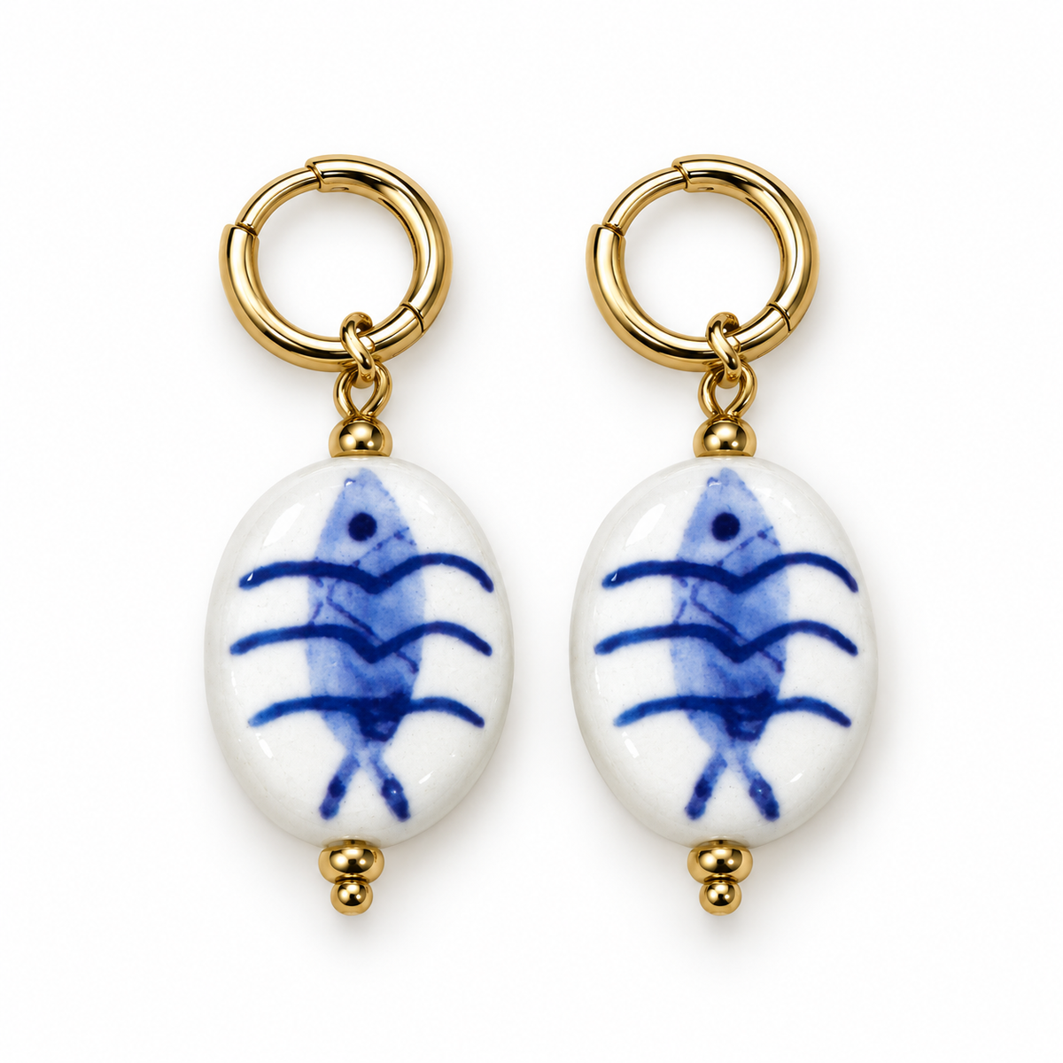 Pendientes de cerámica blanca con pez azul y aro dorado sobre fondo blanco